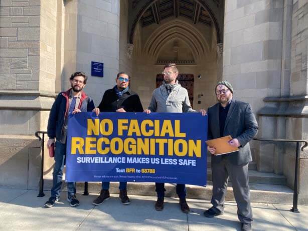 Facial recognition protesters hold up a banner.